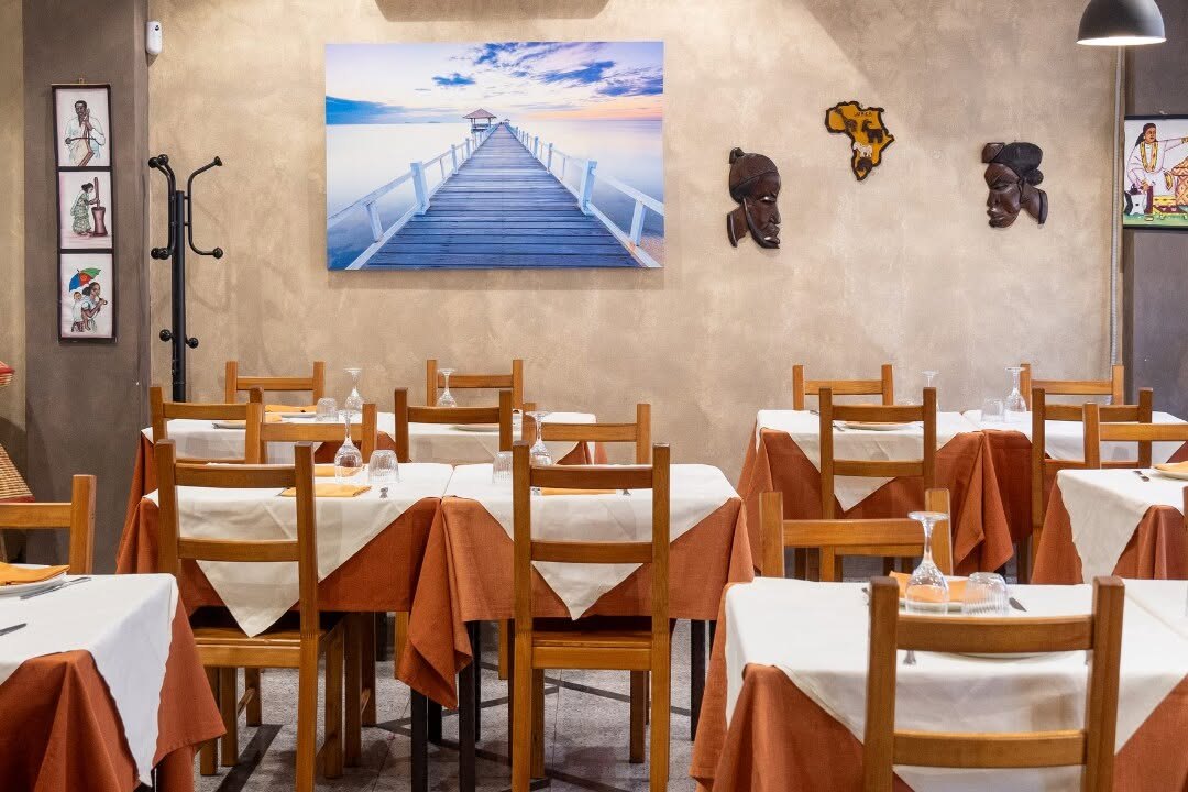 La sala del ristorante con i tavoli apparecchiati, le sedie in legno e un quadro alla parete.